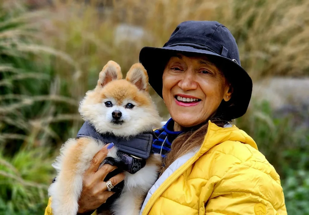 Yvonne wearing a yellow jacket and holding a small dog outside